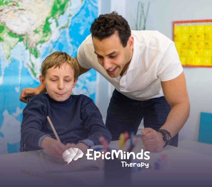 A smiling adult assists a child in a wheelchair with painting in a classroom setting. A world map and colorful calendar are visible in the background.