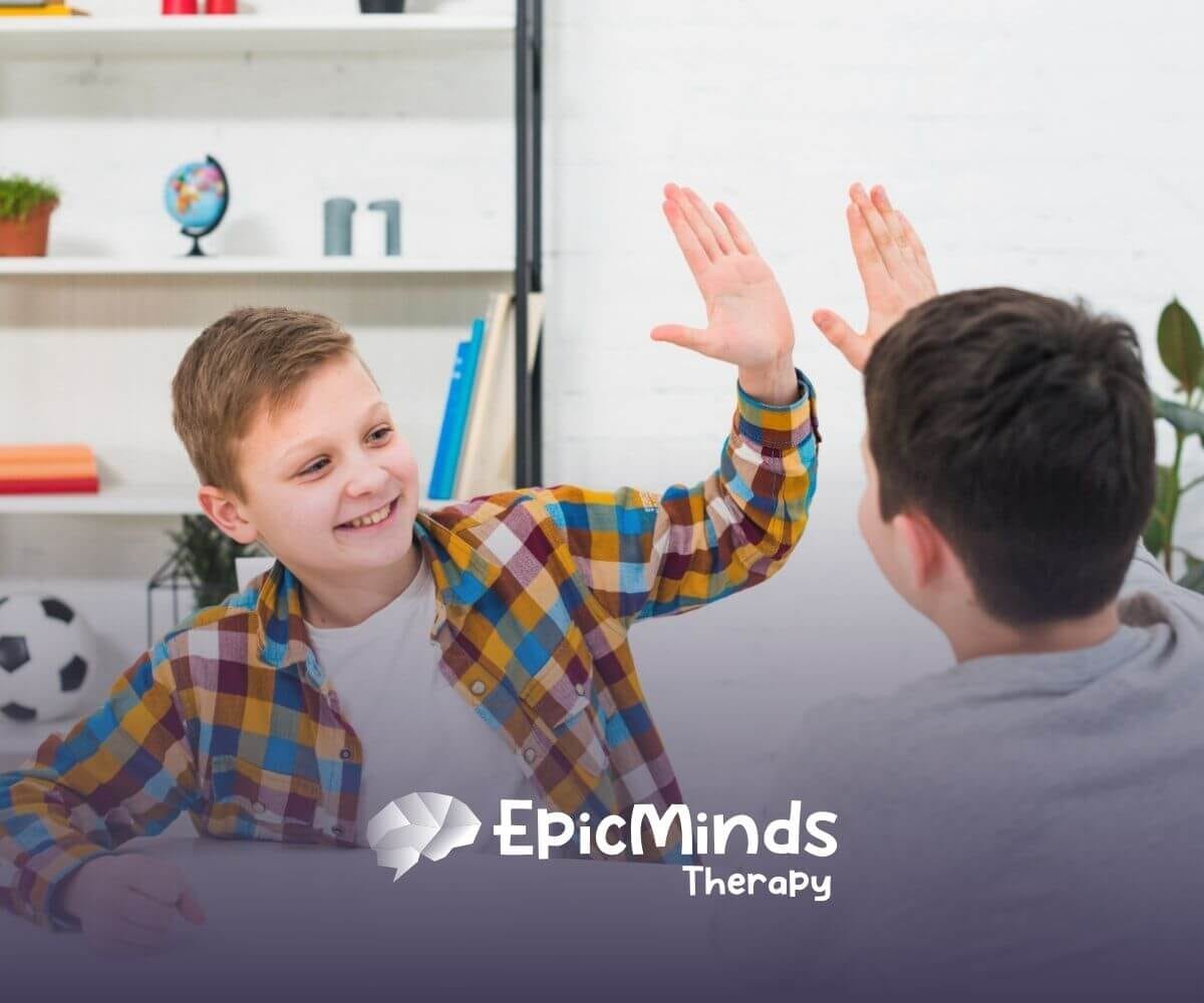 Two boys smiling and giving each other a high five while sitting at a table.