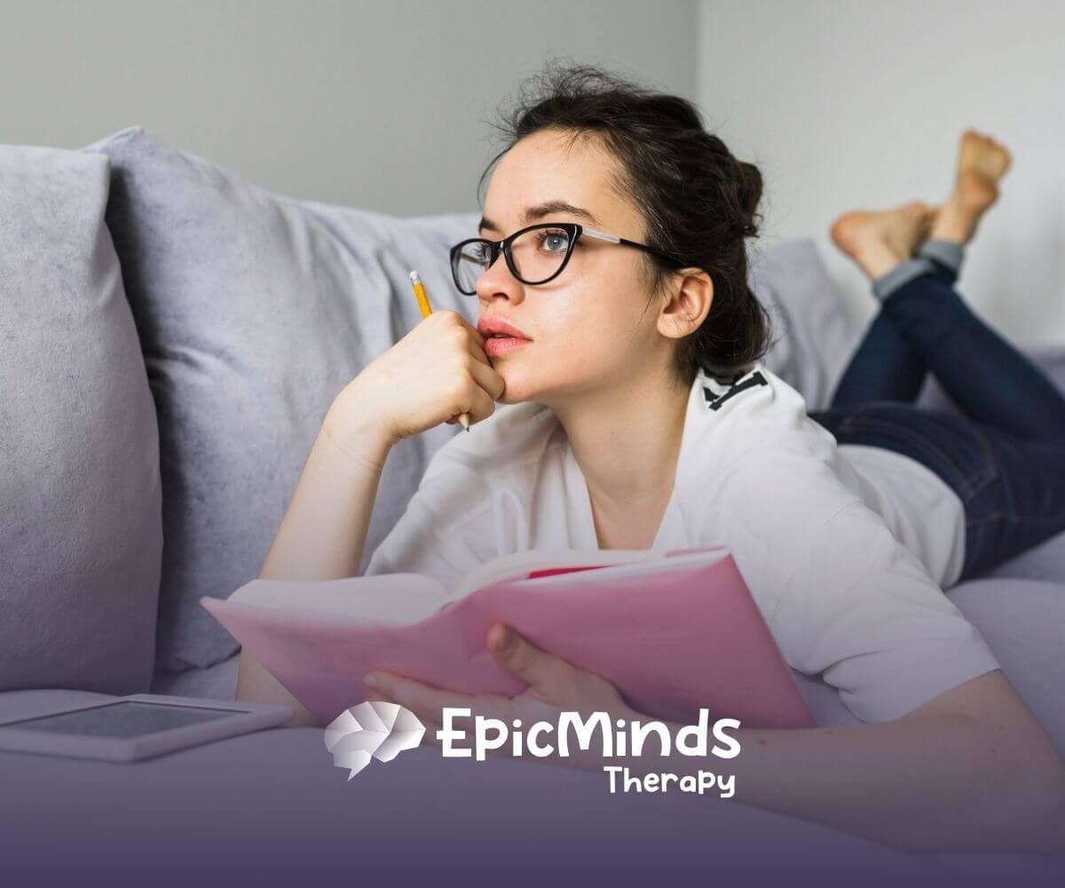 A young woman on the autism spectrum with glasses lies on a couch.