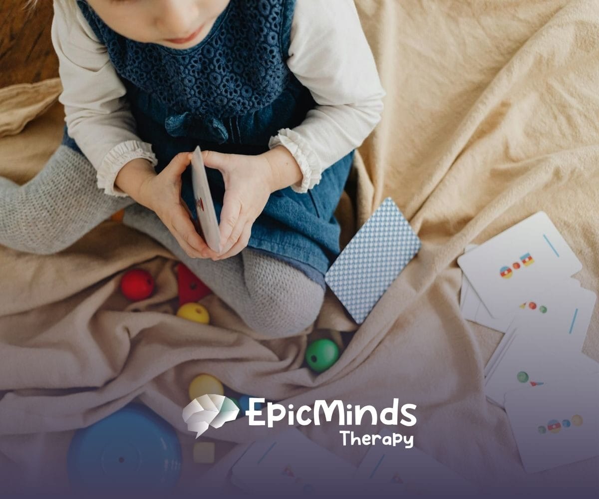 An autistic toddler sitting on a blanket playing with flashcards and colorful toys during ABA therapy in NC.