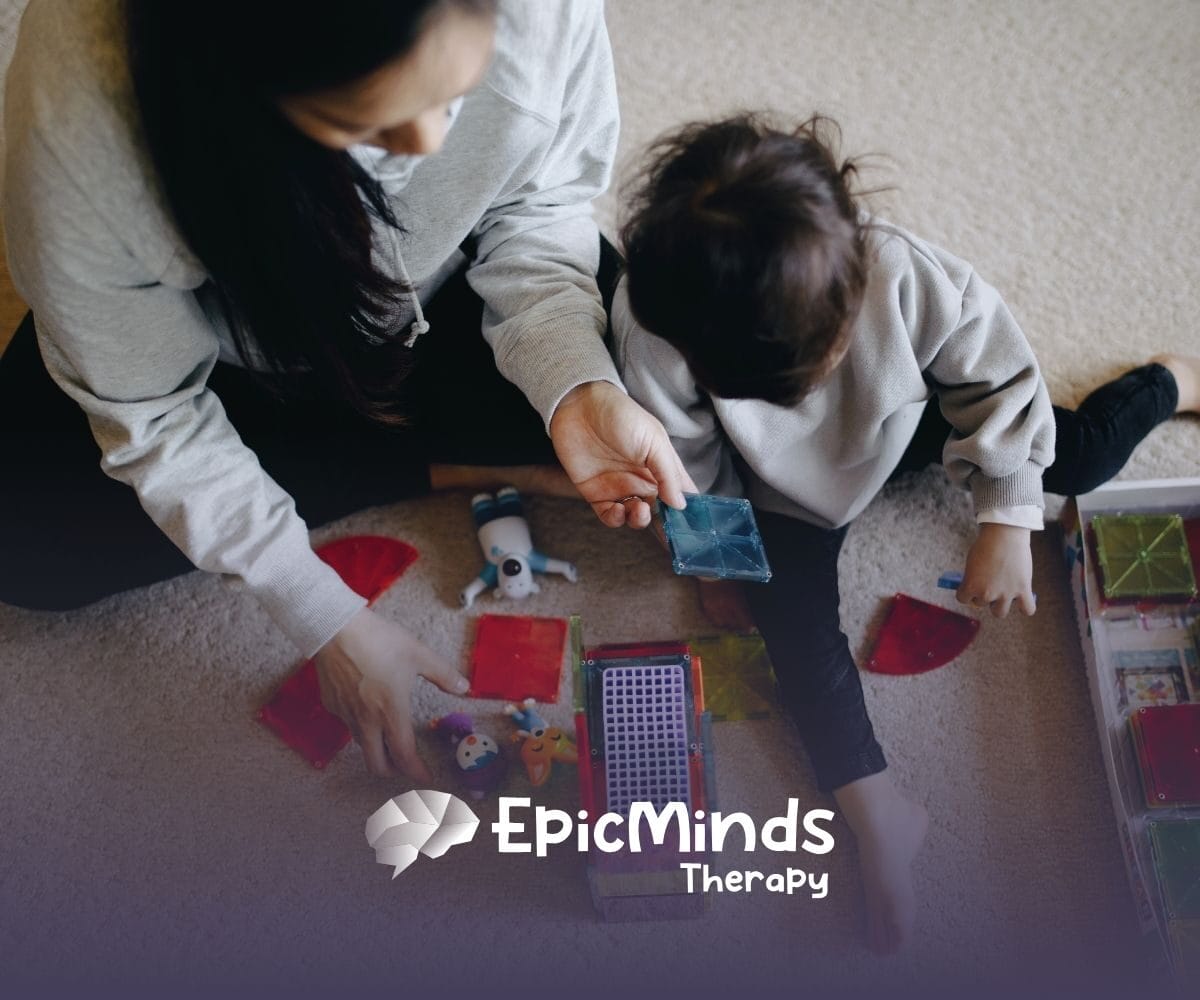 A caregiver and child play with colorful magnetic tiles on a carpet. The scene is cozy and engaging, suggesting learning and creativity.