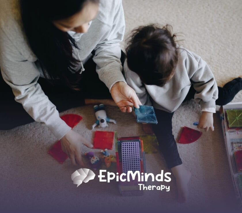 A caregiver and child play with colorful magnetic tiles on a carpet. The scene is cozy and engaging, suggesting learning and creativity.