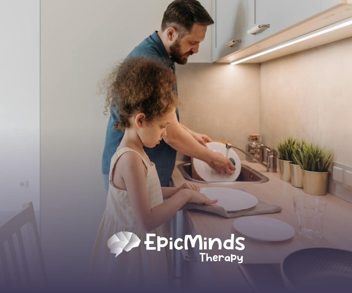 An ABA therapist and autistic child washing and drying dishes together in the kitchen during in-home ABA therapy in NC.