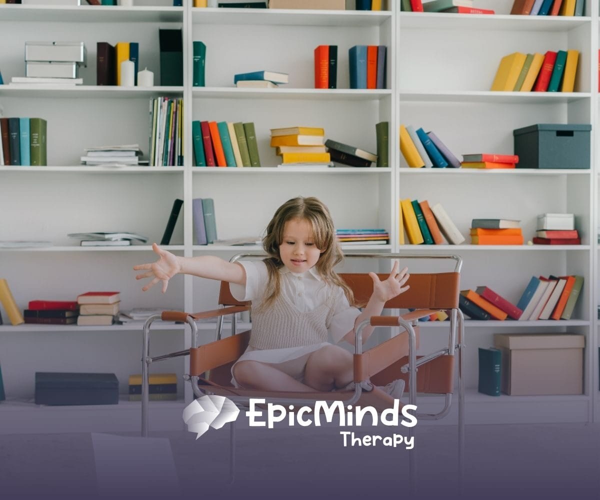 A young girl sits cross-legged on a brown chair in a library, reaching out with an engaged expression. Shelves behind her are filled with colorful books.