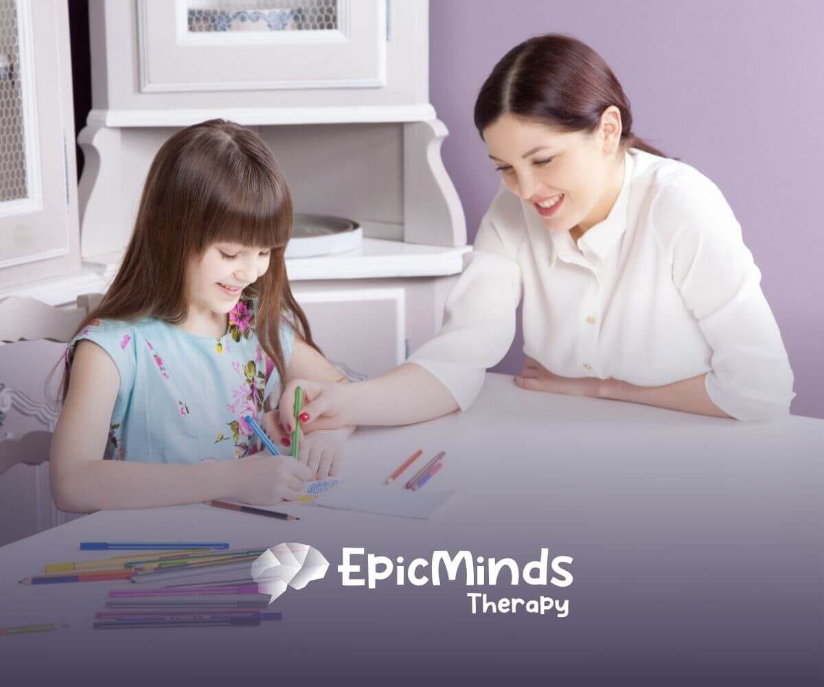 An ABA therapist smiles while guiding an autistic girl in drawing with colored pencils during ABA therapy.