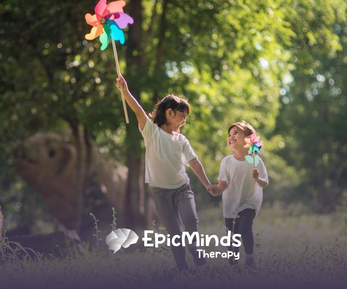 Two children with autism holding hands and playing with pinwheels outdoors.