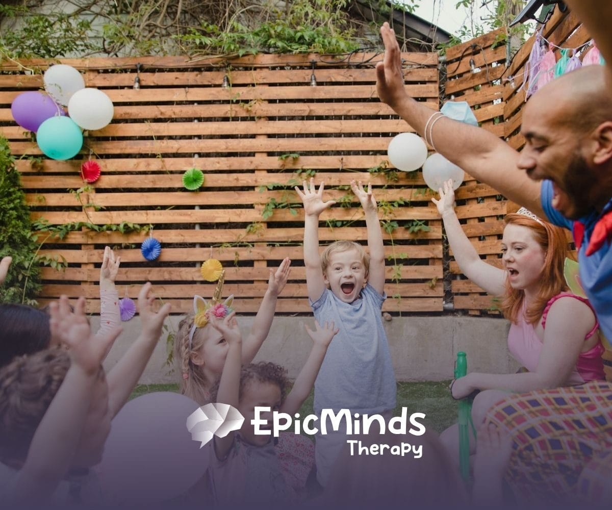 Group of autistic children, RBTs, and BCBAs raising hands joyfully during play-based ABA therapy in North Carolina.