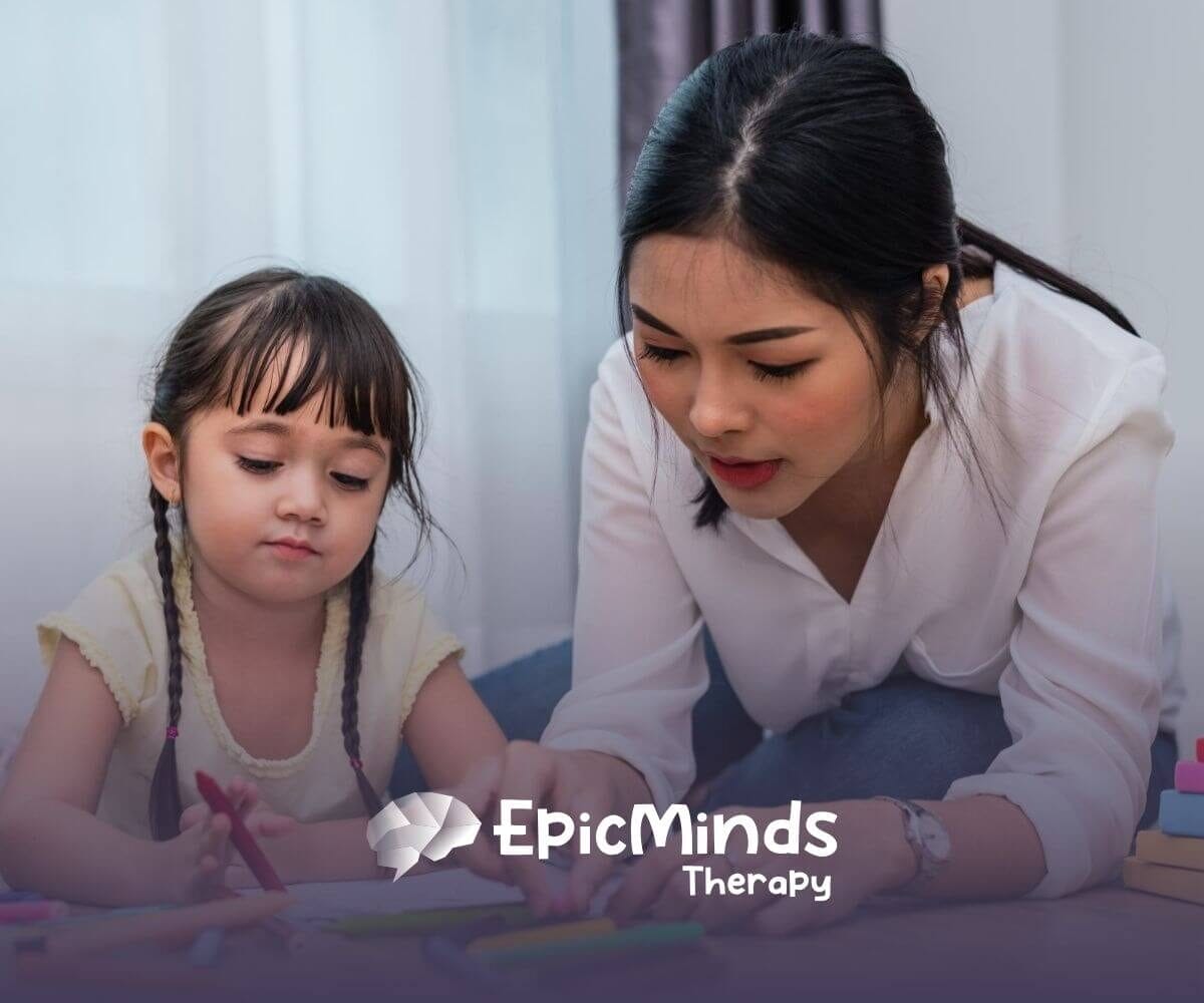 Female BCBA helping autistic girl with coloring activity on the floor in ABA therapy.
