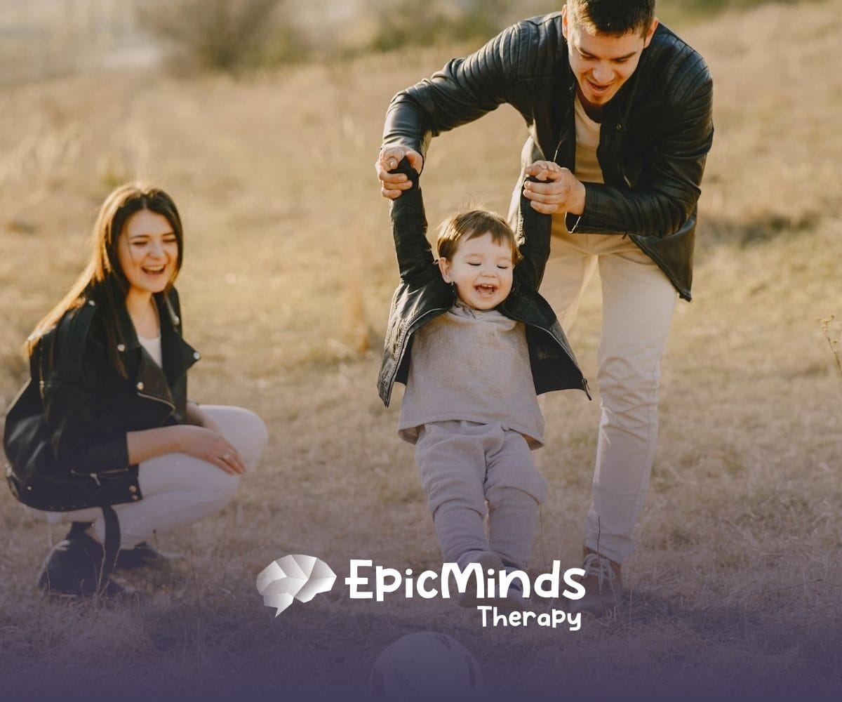 Mom and dad kick a ball with their giggling child in a grassy field on a sunny afternoon in North Carolina.
