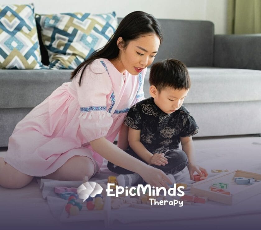 ABA therapist and young autistic kid are playing with wooden educational toys on the floor during ABA therapy in NC.