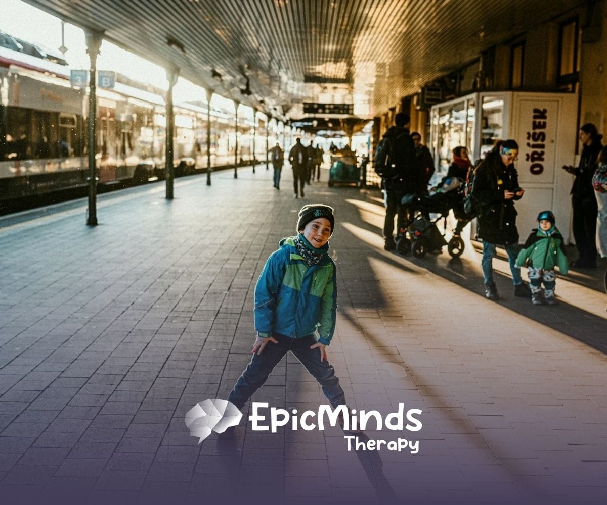 Smiling boy strikes a playful pose on a busy train platform filled with travelers and sunlight in North Carolina.