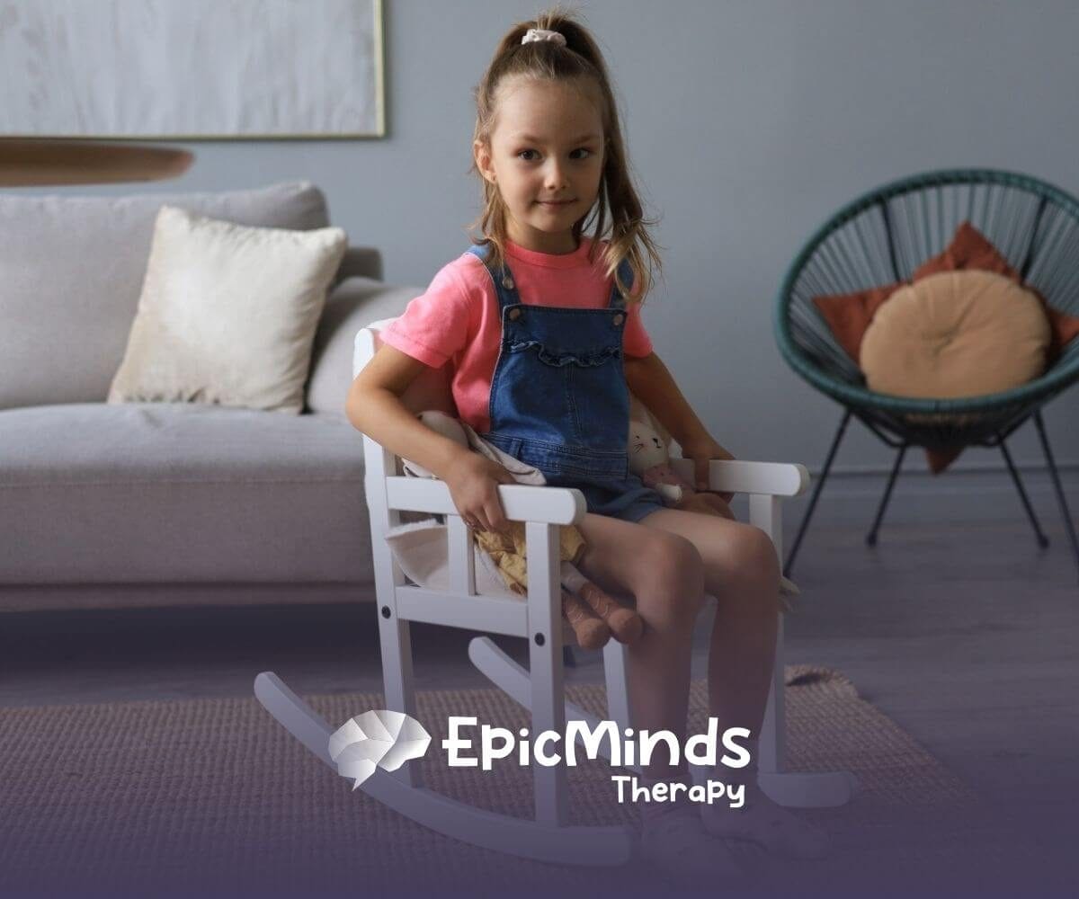A young girl with autism sitting and rocking in a small white rocking chair indoors.