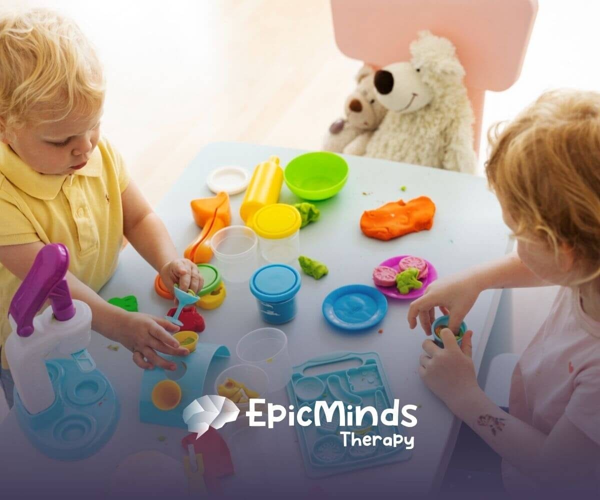 Two children with autism playing with colorful playdough and plastic tools on a table.