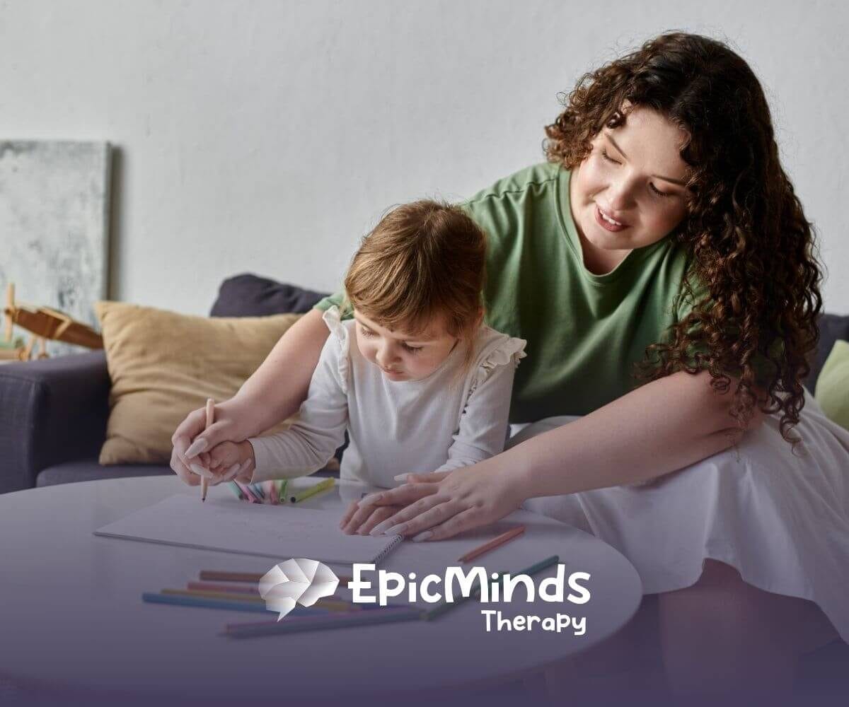 A BCBA helping a girl with autism color in a drawing, with crayons scattered around the table.